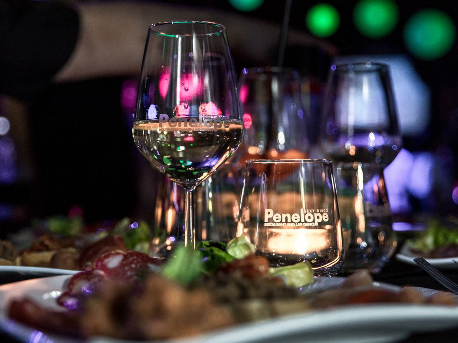 Tavolo apparecchiato con piatti eleganti e calice di vino, atmosfera soffusa fucsia sullo sfondo